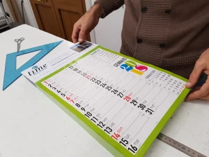 Controllo di un calendario planning da parete sul banco, con squadra e forbici