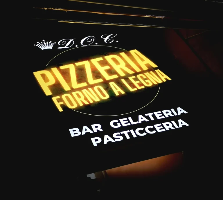 Insegna luminosa a cassonetto di pizzeria, bar e gelateria, fotografata di sera