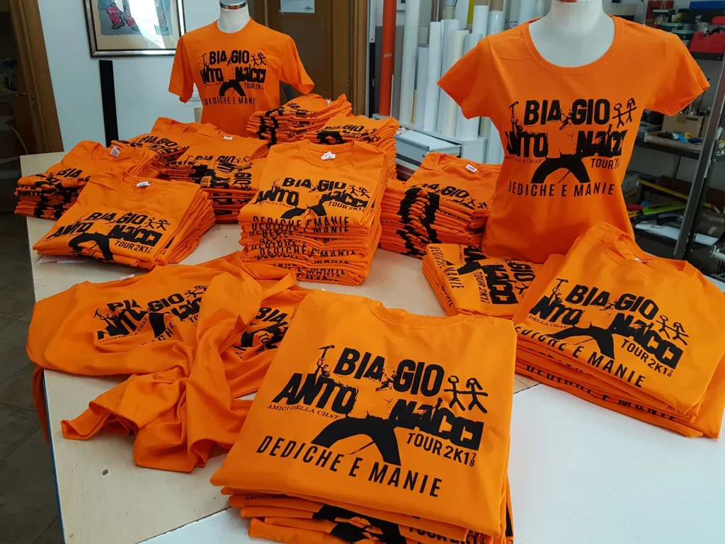 Magliette arancioni serigrafate per il fan club di un tour musicale, stese sul banco