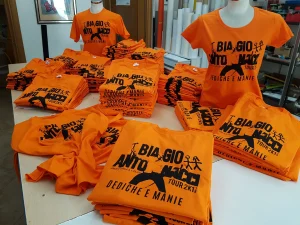 Magliette arancioni serigrafate per il fan club di un tour musicale, stese sul banco