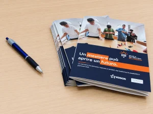 Pila di pieghevoli a tre ante «Un mestiere può aprire un futuro» della Scuola dei Mestieri dell'Energia, finiti sul banco di lavoro accanto a una penna